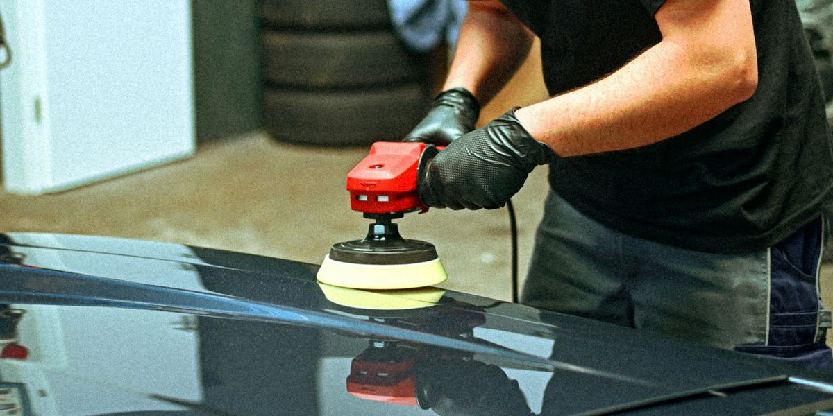 Iemand poetst de motorkap van een donkere wagen met een poetsmachine