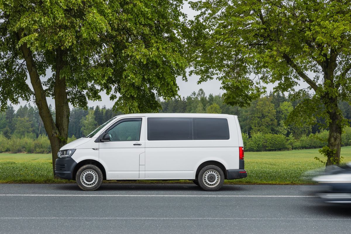 Een witte bestelwagen geparkeerd langs een weg met bomen